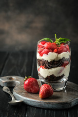 Trifles with fresh strawberries, chocolate biscuit and gentle cream on a dark background.