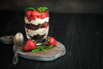 Trifles with fresh strawberries, chocolate biscuit and gentle cream on a dark background.