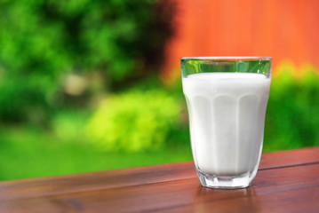 A glass of milk on the background of the summer garden on a wooden table.