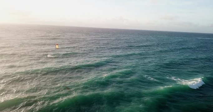 Aerial shot, showing a kite surfer riding towards the sunset in Barbados, a carribean island.