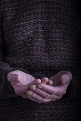 Fototapeta premium The palms of an old person in a dark, rough sweater are folded together, a concept of help, care and health, a background or concept
