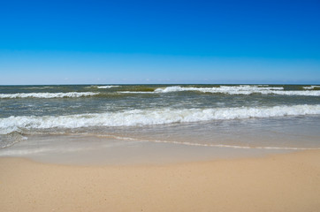 Sea waves wash the clean sandy beach. Landscape on a wild beach. The sea in the summer.