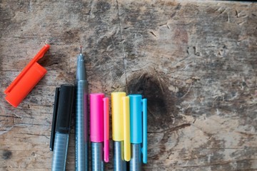 Multiple colored pens grouped together on a rustic wooden table or desk