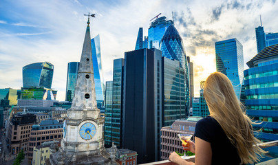 Aerial view of skyscrapers of the world famous bank district of central London at sunset and woman drinking cocktail and enjoying the vi
