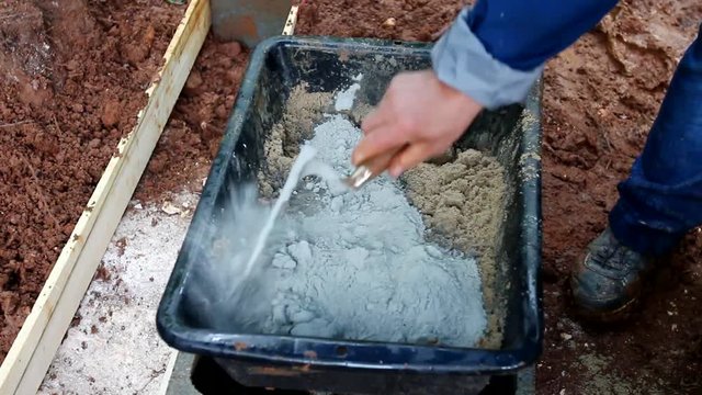 Man mixing sand and cement with a trowel in a tub. Manual preparation of concret. 