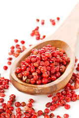 Pink or rose brazilian red peppercorns (schinus terebinthifolius) in wooden spoon over white