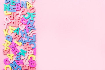 Many multicolored wooden letters on a pink background. toy letters. english alphabet. View from above. Flat lay. Copy space for text - obrazy, fototapety, plakaty