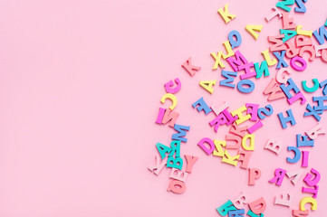 Many multicolored wooden letters on a pink background. toy letters. english alphabet. View from above. Flat lay. Copy space for text - obrazy, fototapety, plakaty