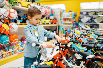 Little boy buying bicycle in kids store, side view