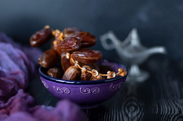 Branch of dates fruit in the purple plate with purple and black wooden background. Eastern sweets. Healthy snack. Dried dates