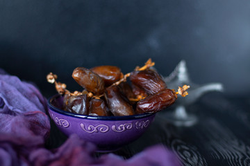 Branch of dates fruit in the purple plate with purple and black wooden background. Eastern sweets. Healthy snack. Dried dates