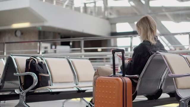 Blonde woman with luggage holding smartphone.