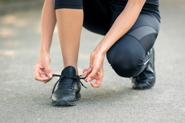 Women's hands lace up black sneakers, a symbol of preparation for running or sports