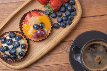 fruit tartlets on a wooden plate and cup of coffee on the table, fruit baked shell, fruit cupcake with berry