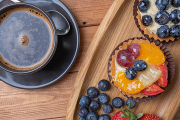 fruit tartlets on a wooden plate and cup of coffee on the table, fruit baked shell, fruit cupcake with berry