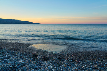 The sunset on the pebble beach with hills on the background, Kolymbari, Crete, Greece.