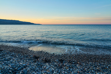 The sunset on the pebble beach with hills on the background, Kolymbari, Crete, Greece.
