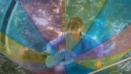 Happy child inside a balloon. Happy little girl have fun in an inflatable ball on the water.