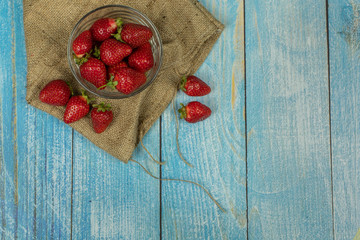 Strawberries in small glass plate on blue wooden table. Place for logo or text