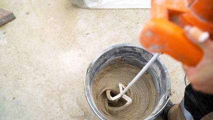 mixing concrete plaster with electric mixer. Stir the solution in a bucket.