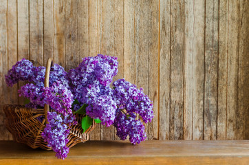 basket with a bouquet of flowers of lilac on a wooden background. soft focus.