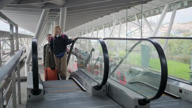Traveling couple on airport escalator with baggage.