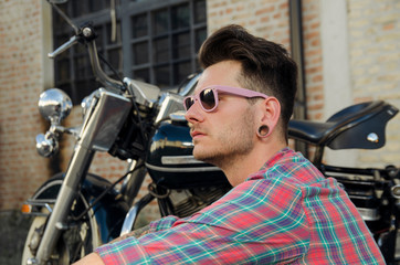 Fototapeta na wymiar Closeup portrait hipster man sitting next to a motorcycle 