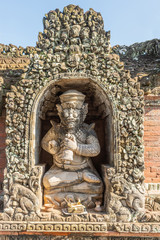 Ubud, Bali, Indonesia - February 26, 2019: Batuan Temple. Niche with man holding bell. Red bricks and gray stone ornaments covered with green and black mold.