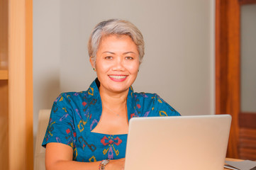  Lifestyle portrait of Happy and attractive elegant middle aged Asian business woman working smiling at office computer desk feeling positive and successful