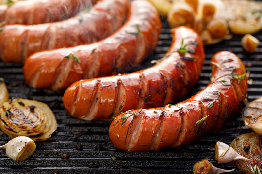 Grilling sausages with the addition of herbs and vegetables on the grill plate, close-up. Grilling food, bbq, barbecue
