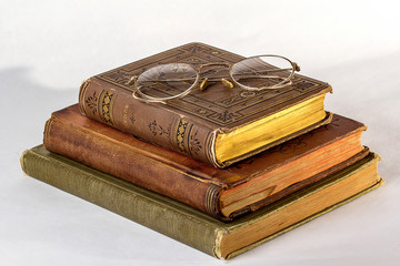 Stack of Three Antique books with a pair of vintage eyeglasses on a white background.