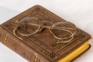 A pair of Antique Eyeglasses sitting on a vintage hymnal on a white background.