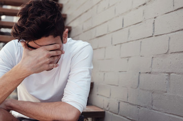 Depressed young adult man sitting alone, mental illness health concept