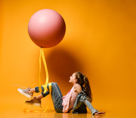Young beautiful teenager girl posing on a yellow background, lies and holds up a huge giant pink balloon. Summer style.