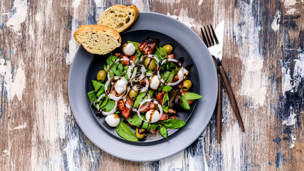 Mediterranean salad with fresh green salad with mozzarella, tomatoes, olives, onion and balsamic dressing. Italian traditional cuisine. Top view. Food banner