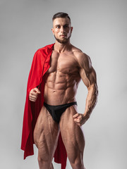 Male bodybuilder puts on his shoulders a red cloak with a serious face