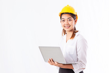 Beautiful young Asian woman wearing yellow safety helmet. Architect woman using laptop and smiling while standing at her working place with white background and copy space.