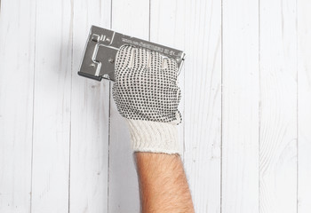 Tool. Hand in glove is holding industrial stapler on a white wooden background .
