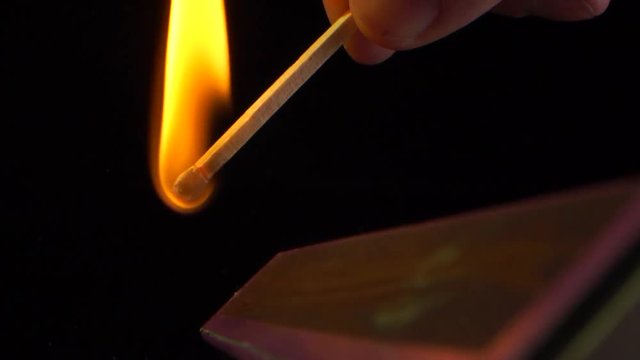 Beautiful match-fire Ignition and burning in slow motion of a match on the side of the box, black background.