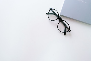 Black eye glasses are placed on a stack of books on a white wooden table beside the window.