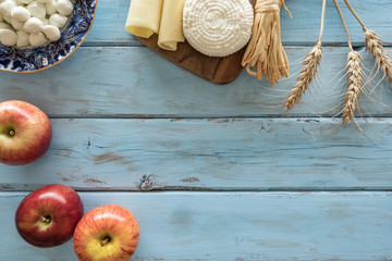 Top view of dairy products, stalks of wheat, apples on a blue background. Symbols of jewish holiday - Shavuot.