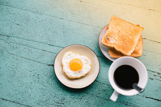 Fried eggs, toast, coffee, breakfast set placed on a blue wooden table  Photos | Adobe Stock
