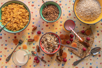 Bowls full of cereals, fruits scattered around the table and a glass of breakfast milk