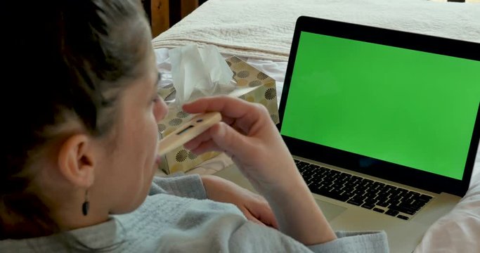 Woman taking her temperature with a thermometer with a green screen computer