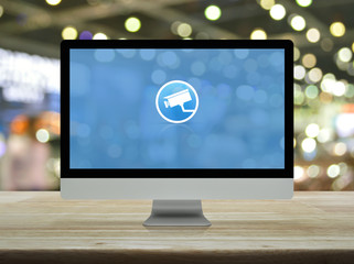 cctv camera flat icon on desktop modern computer monitor screen on wooden table over blur light and shadow of shopping mall, Business security and safety online concept