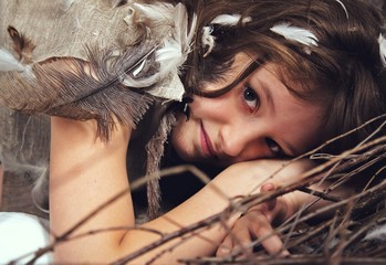 girl with long brown hair in a linen dress with feathers ,lying in the fetal position in a decorative nest of branches with decorative white eggs. close-up portrait