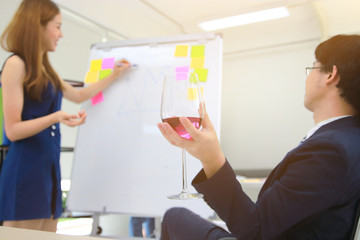 Selective on hands of executive holding a glass of wine with confident young Asian business woman explaining strategies on flip chart in boardroom