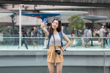 Attractive young Asian woman taking photo or selfie outdoors in urban