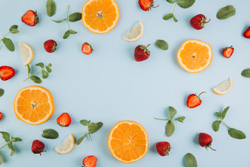 Summer colorful flat lay. Pattern made of citrus fruits, leaves and strawberries on the blue wooden table. Top view and copy space