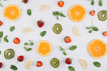 Summer colorful flat lay. Pattern made of citrus fruits, green kiwi, leaves and strawberries on the white wooden table.